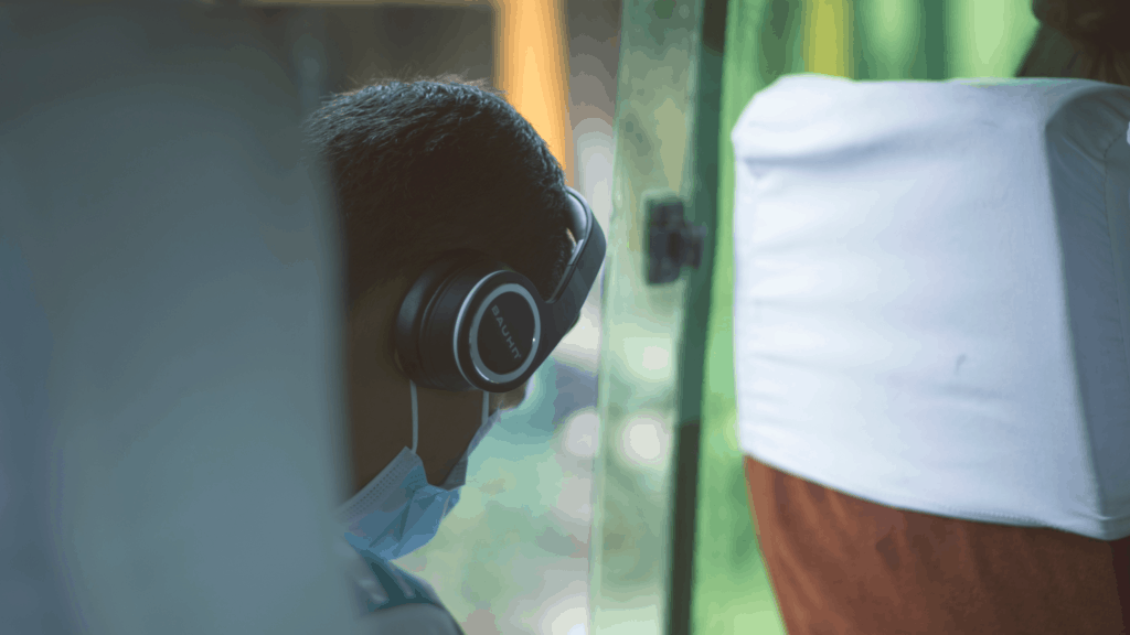 Person wearing mask on public transit, using their phone and wearing headphones.