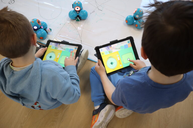 Two boys sitting on the ground, with tablets in their hands. Dash and Dot GO is on the tablet screen.
