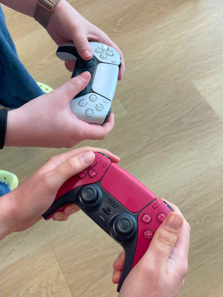 Two youth holding a red PS5 controller and a white PS5 controller.