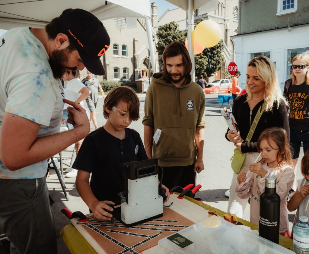 STEAMFEST-feature-image An ampere employee standing to the left of the screen is overlooking a student playing with coding activities. On lookers are seen to the right side.