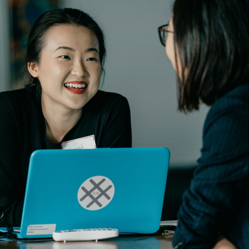 Two people are sitting in front of a computer smiling at each other.