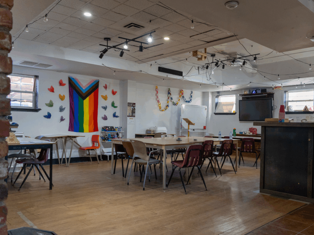 Crafting area of the Bathurst Makerspace and Skills Hub with LGBTQ+ flag on the wall and a conference table with chairs in the background