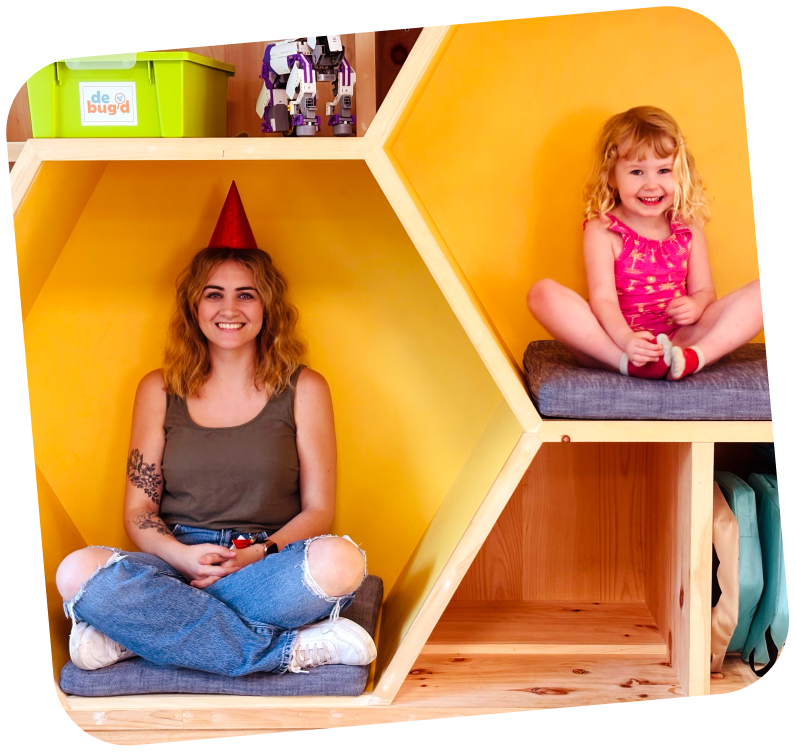 An adult and child sitting in seperate hexagon shaped seating areas with their legs crossed. The adult is wearing a birthday hat.