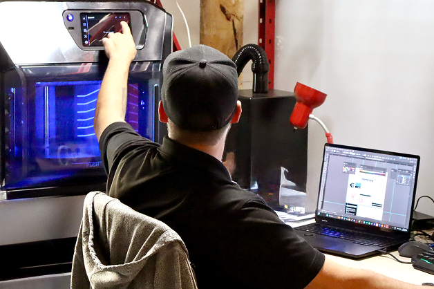 The back of someone who is working on a computer and setting up a 3D printer,