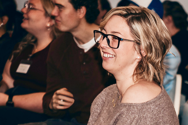 A woman is smiling and facing forward, others are blurred behind her.