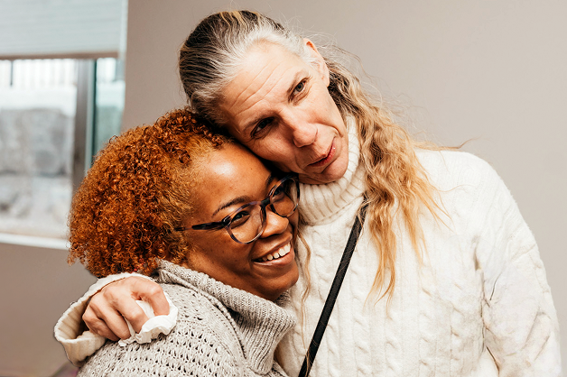 Two woman are side hugging and have big smiles on their faces.