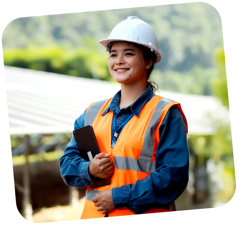 A woman in a hard hat and visibility vest, holding a clip board.