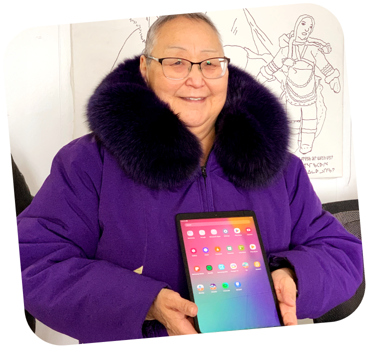 A woman is holding a refurbished iPad that is turned on, she is wearing a purple parka and is smiling wide.
