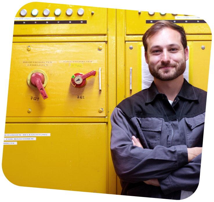 A young man is standing in front of an electrical box that is shut and painted yellow.
