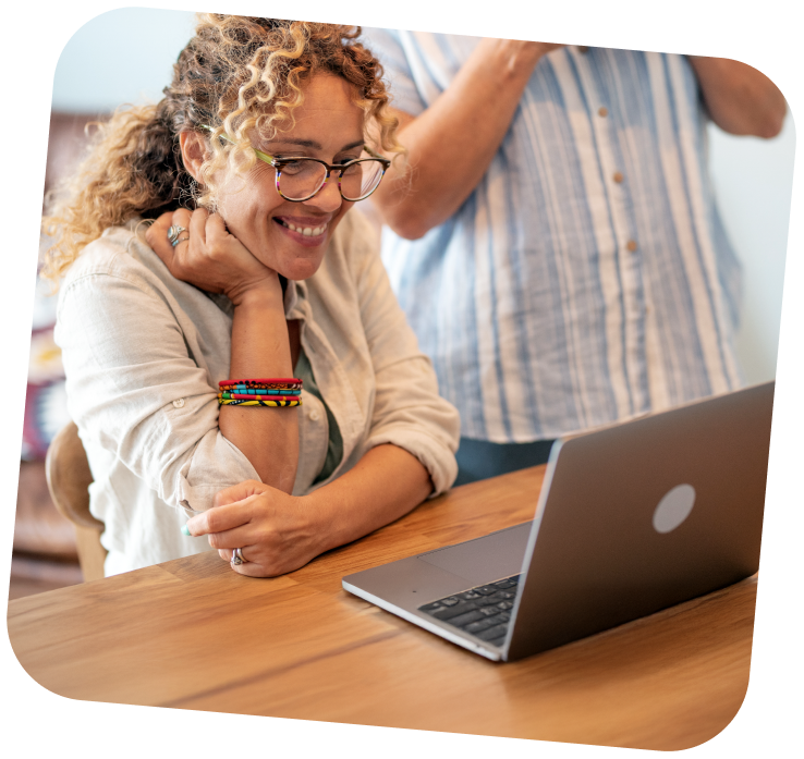 develop-digital-ai-skills-programs-1 A woman is sitting at a table and is smiling widely at her computer.