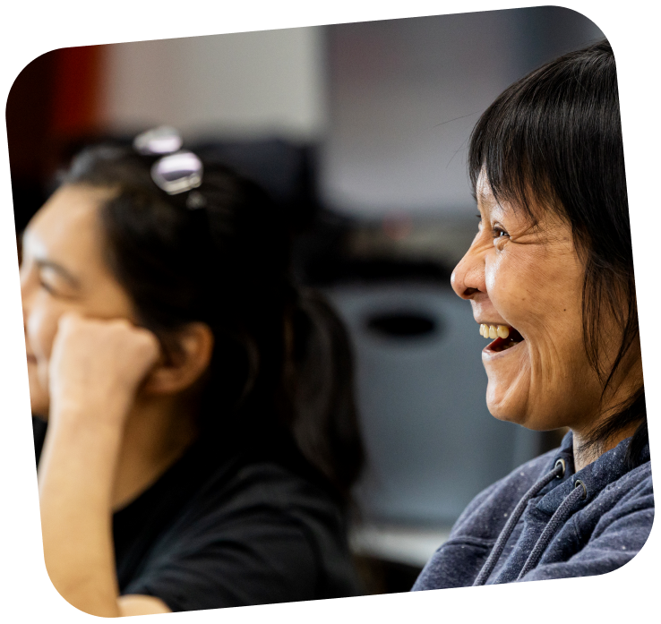 develop-digital-ai-skills-programs-2-Inuit woman learning digital skills Two woman are in the frame, the one near the back is slightly out of focus and leaning on her hand, while the other woman is smiling.