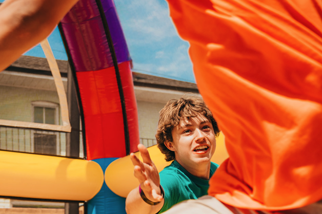 A teen is reaching for another person that is out of view. They are inside a jumping castle.