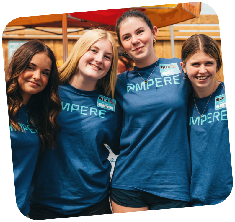Four volunteers standing together outside, they are wearing blue ampere branded shirts with name tags stuck to the right side of the shirt.