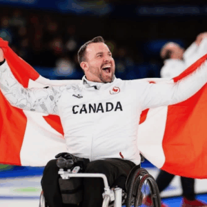 Jon Thurston in his team Canada uniform. He is holding up a Canada flag behind him,