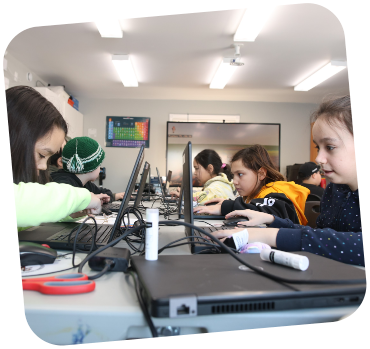A table with two rows of kids on each side. They are all working and looking at their computers.