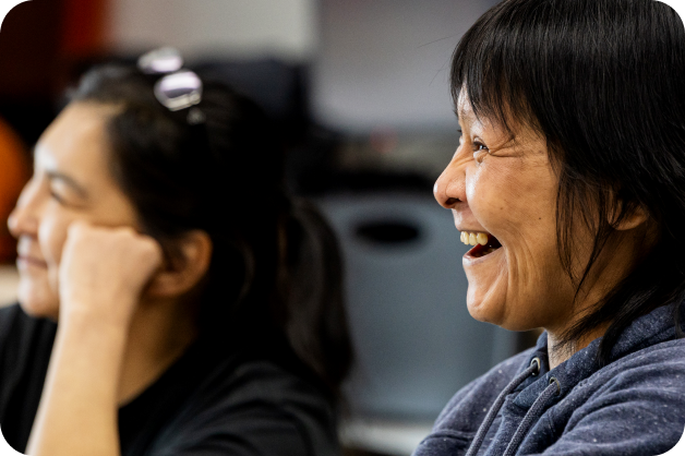 small-business-support-benefits-2-Inuit woman learning digital skills Two woman are in the frame, the one near the back is slightly out of focus and leaning on her hand, while the other woman is smiling.