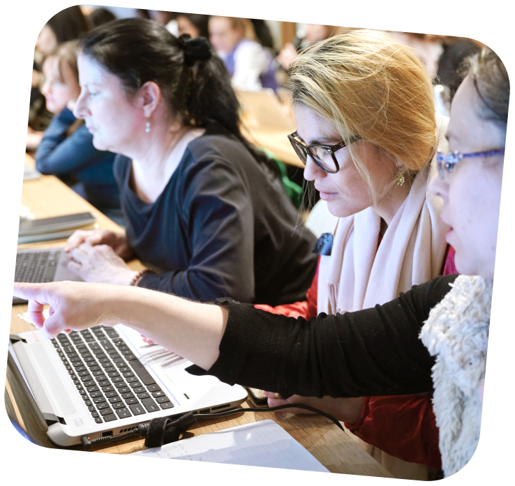 small-business-support-programs-3-adults learning digital skills A row of 3 learners sitting down at a table. The one in the middle is looking at her computer as the person to the left of her is pointing at the computer screen.