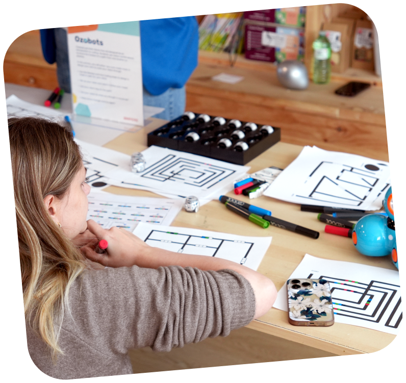 A student sitting at a desk with her back to the camera. Worksheets are spread across the desk.