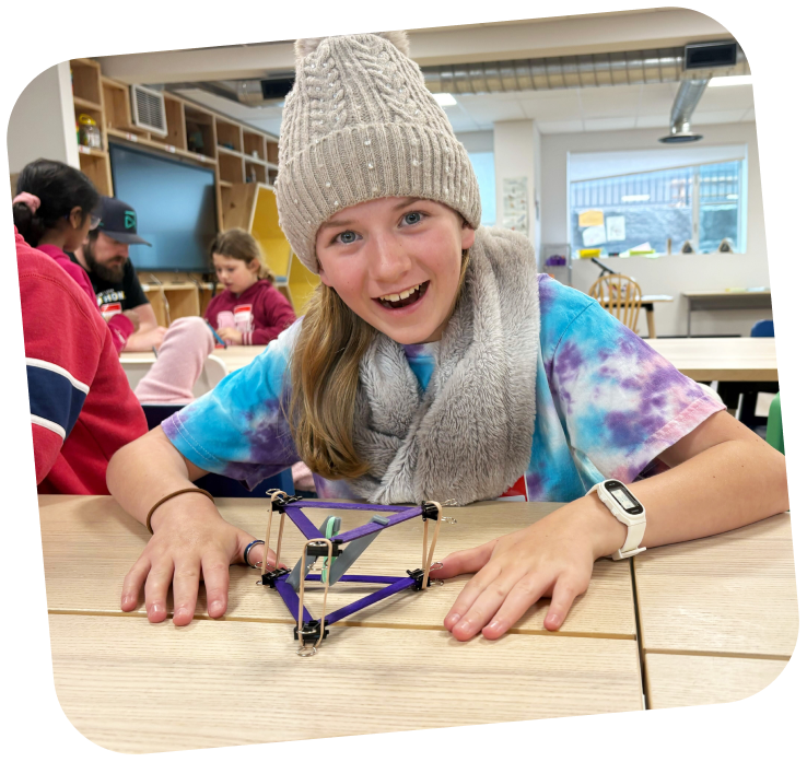 makerspace-teen-steam-project A student smiling at the camera. her hands are on the table and has a creation in front of her.