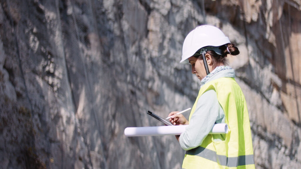 A worker wearing a hard hat with their back to the camera. They are facing a wall of rock.