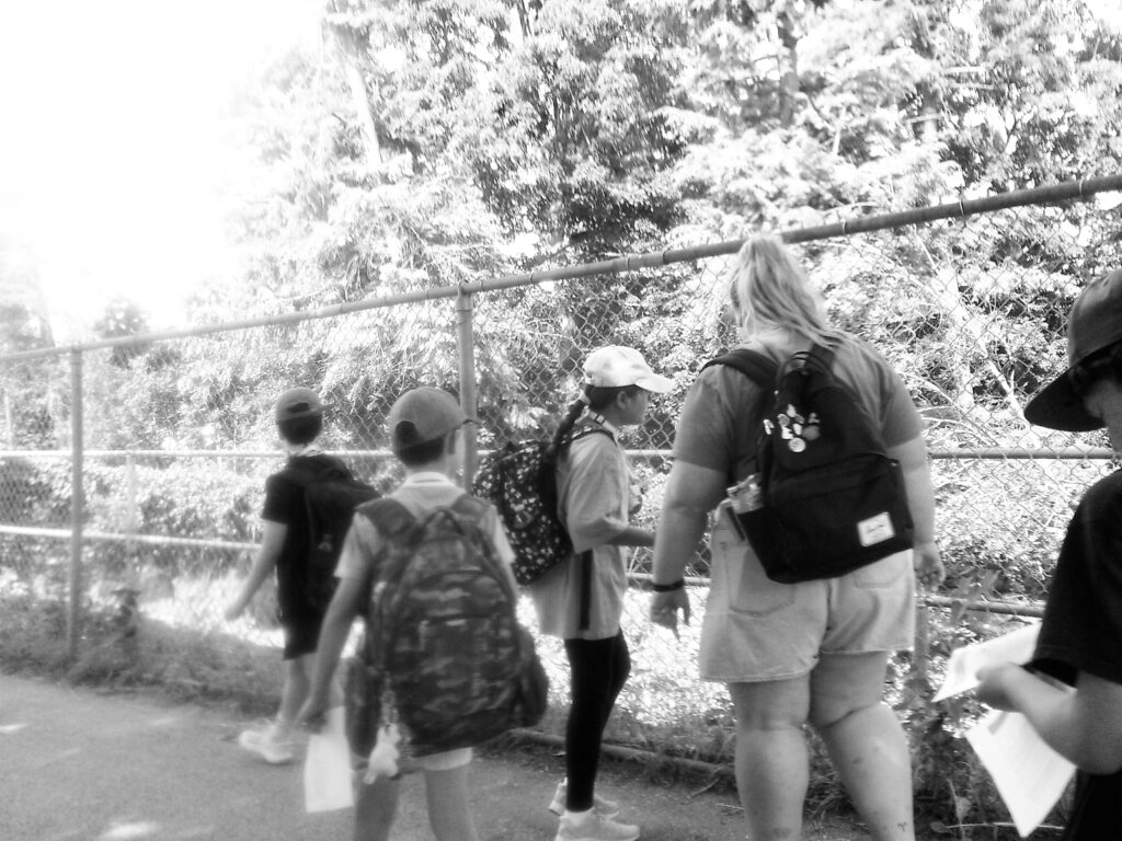A group of people, including a teacher and 4 students, stand at a fence watching animals at the Peterborough Zoo.