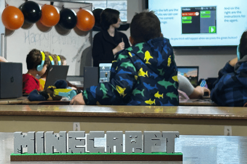 Bathurst Minecraft Camp A 3d printed minecraft logo is in focus, and behind (out of focus) kids are learning basics of coding.