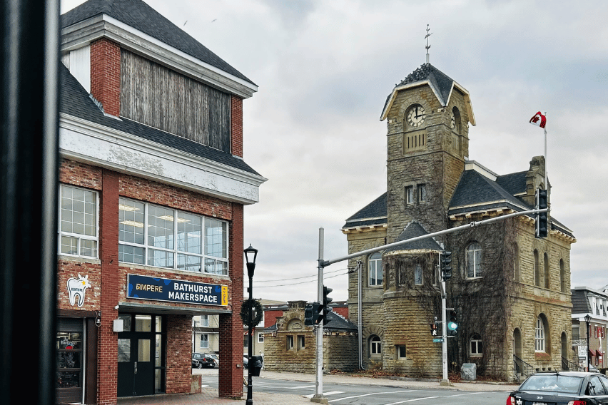 Ampere Bathurst Makerspace An outdoor shot of the Ampere Bathurst Makerspace in Bathurst, New Brunswick. Clearly visible is an intersection with an old post office of gray stone. Another building made of red brick stands, and a sign on that building says Ampere Makerspace.