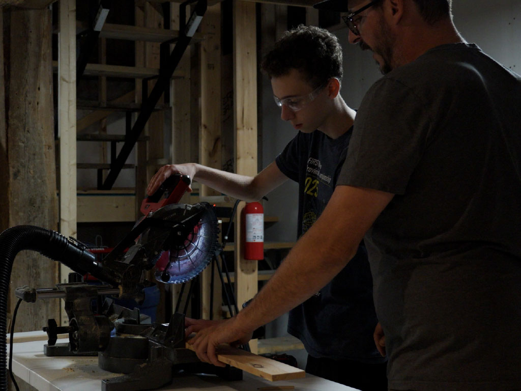 Jamie works with Dan Kitchen, cutting pieces for a bluetooth speaker at a work station.